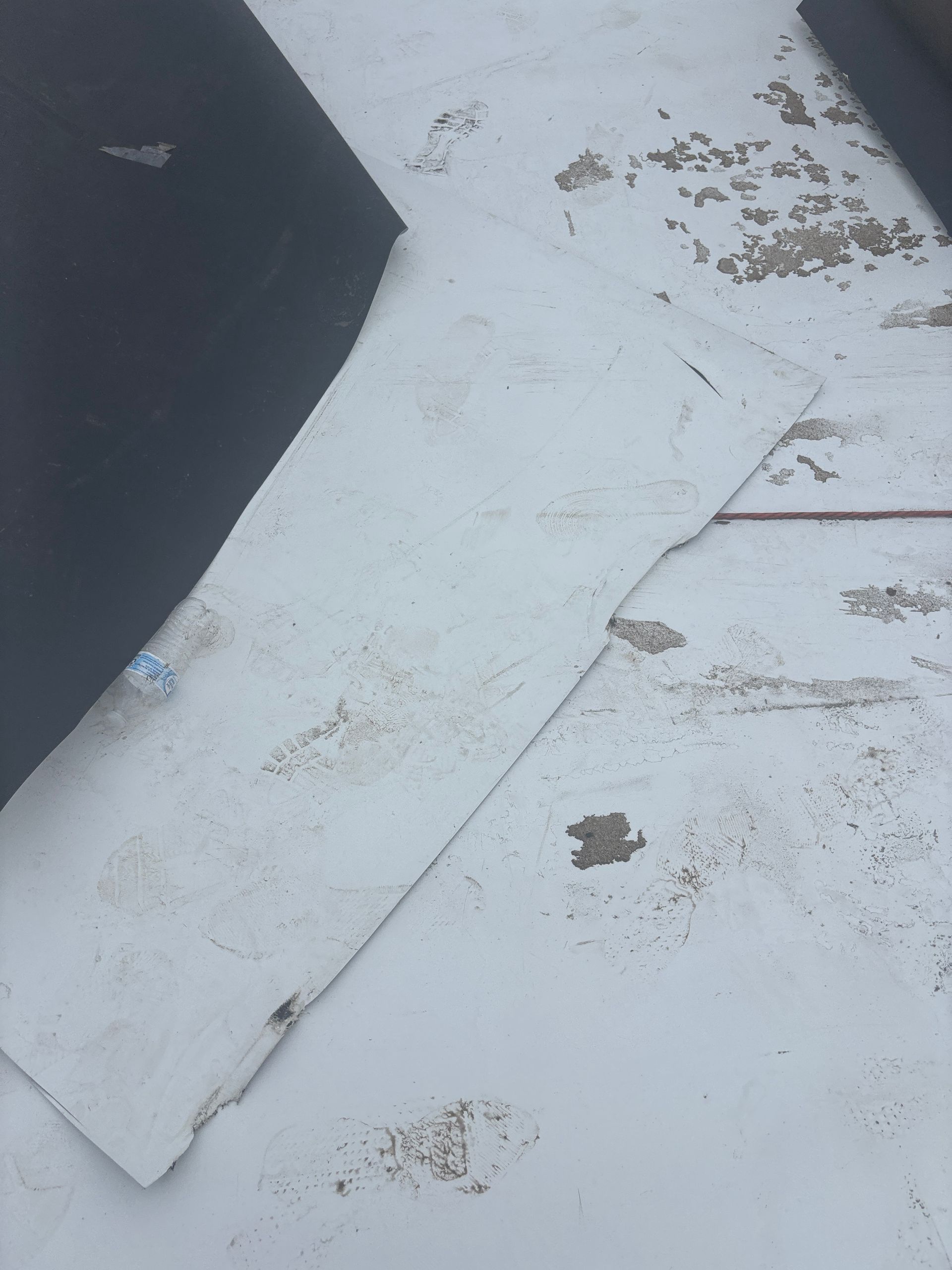 Flat roof surface with peeling white coating and exposed brown patches. Black material partially covers the roof.