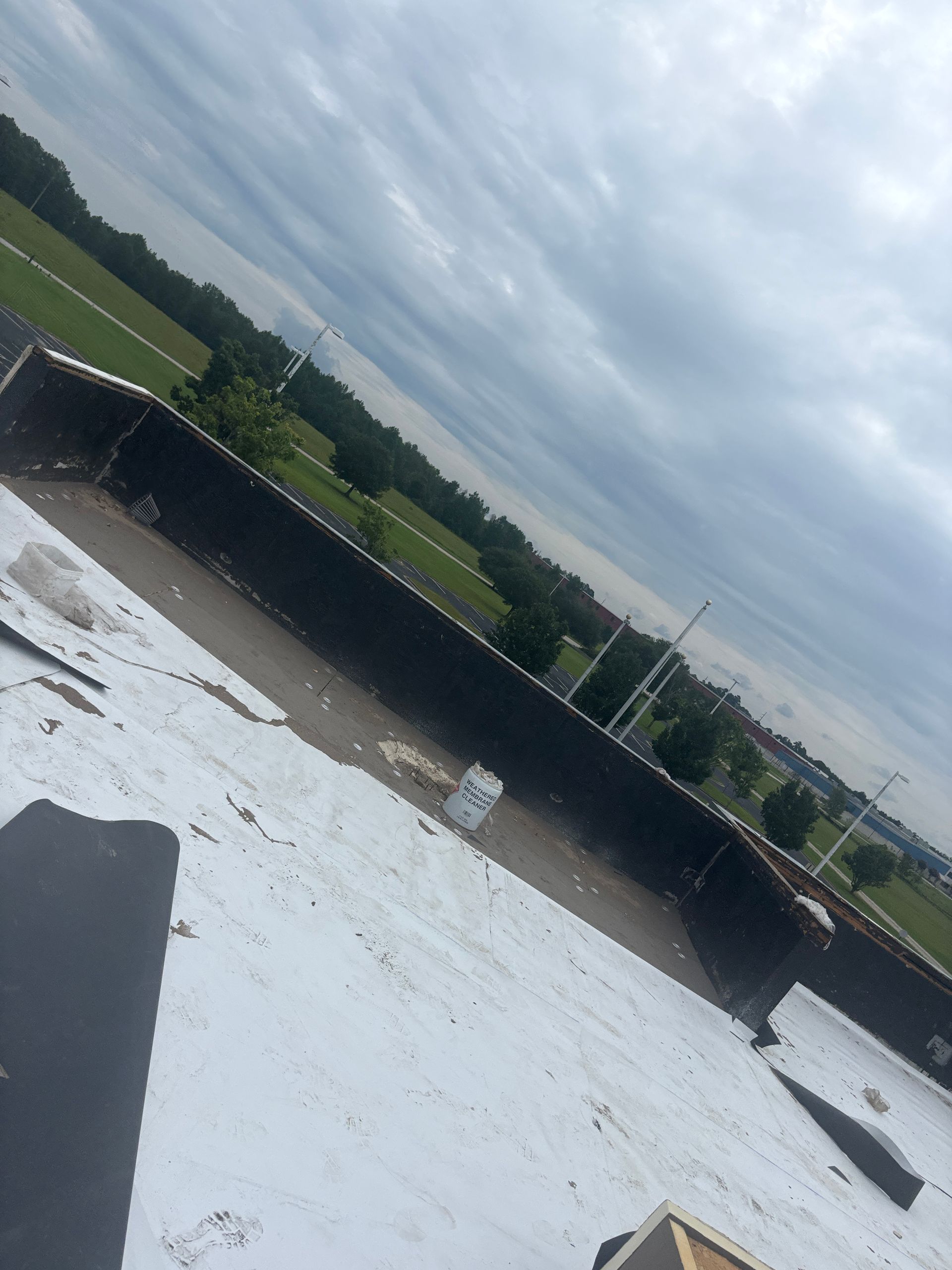Overhead view of a flat roof with a built-in trough filled with water; cloudy sky and green field in the background.