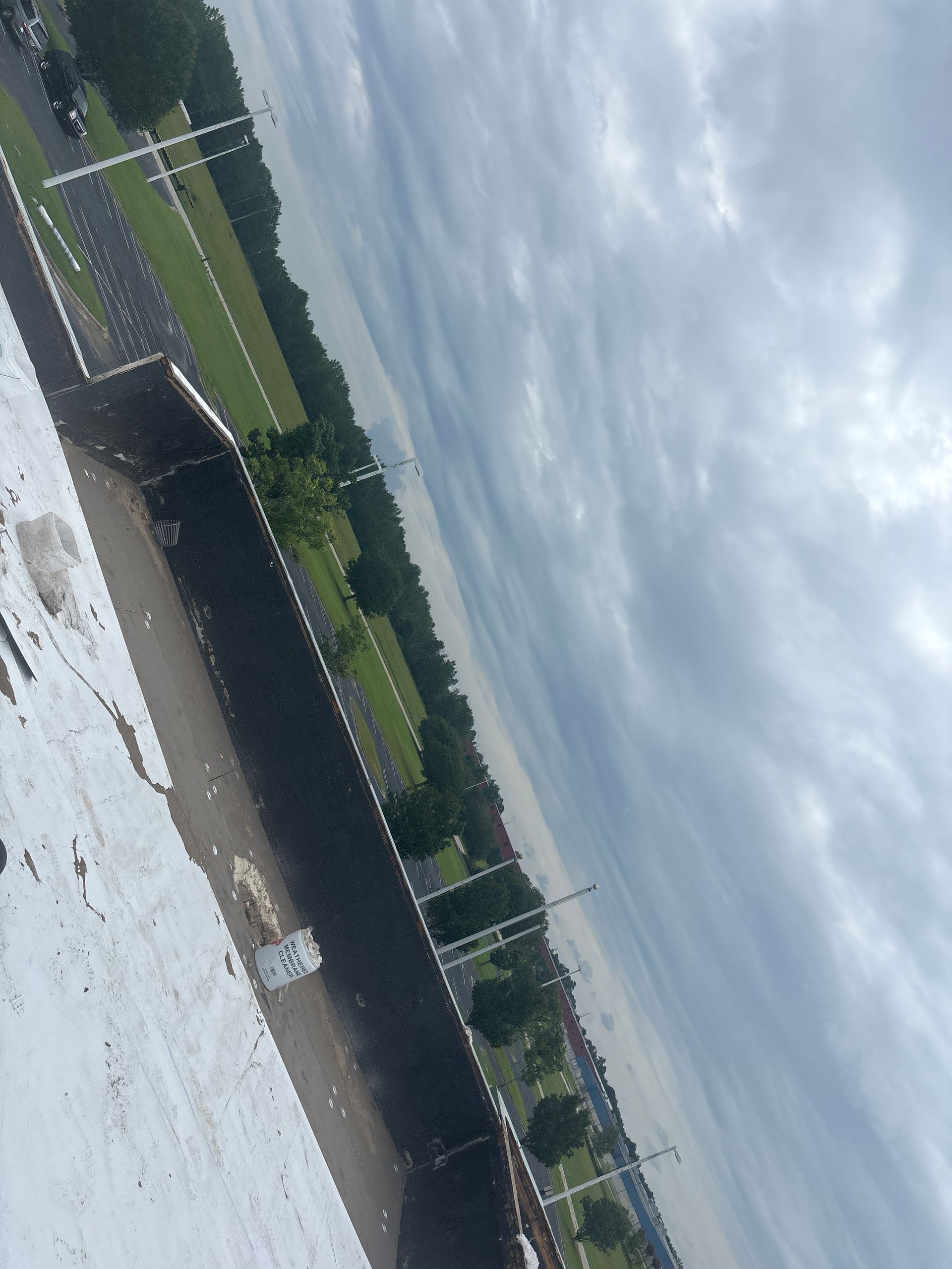 View from above shows a long, grey road lined by a park under a cloudy sky.