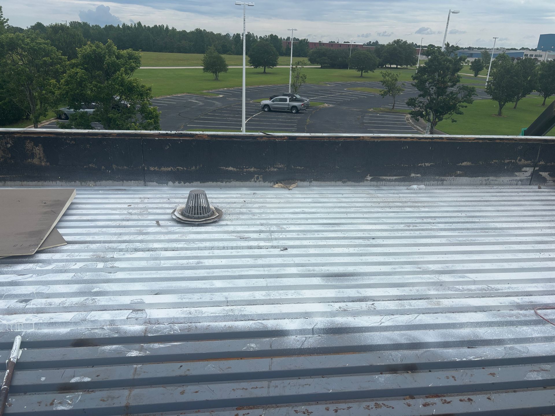 Metal roof with a vent, parking lot in background. Overcast sky.