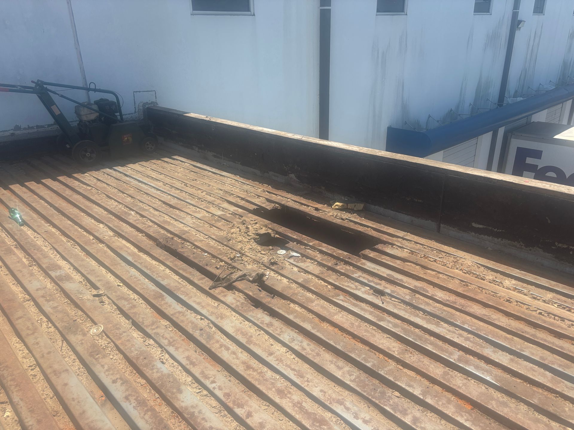 Rusty corrugated metal roof with a damaged area and a white building in the background.