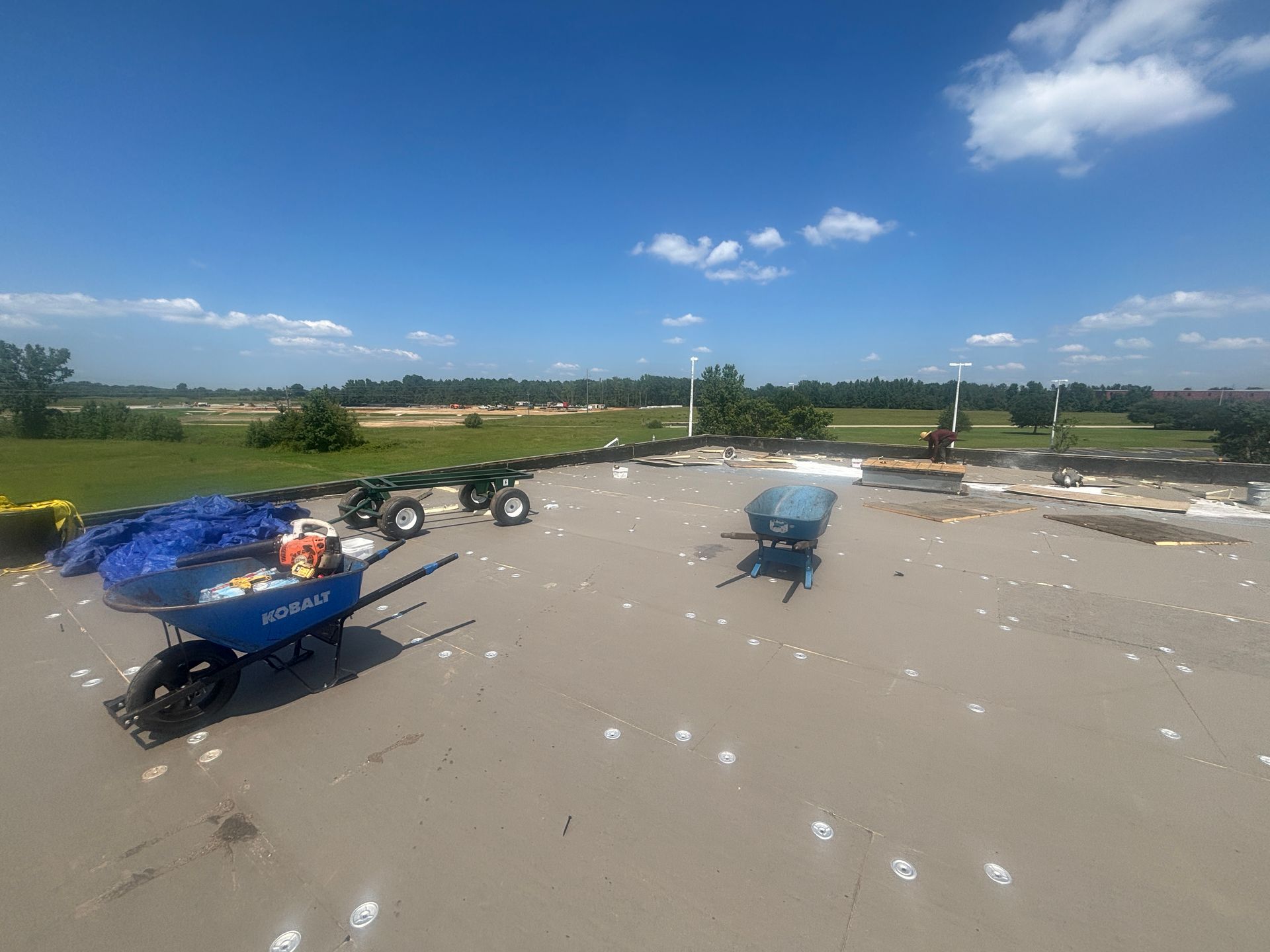 Blue wheelbarrows and small tractors on asphalt with a blue sky and green landscape.