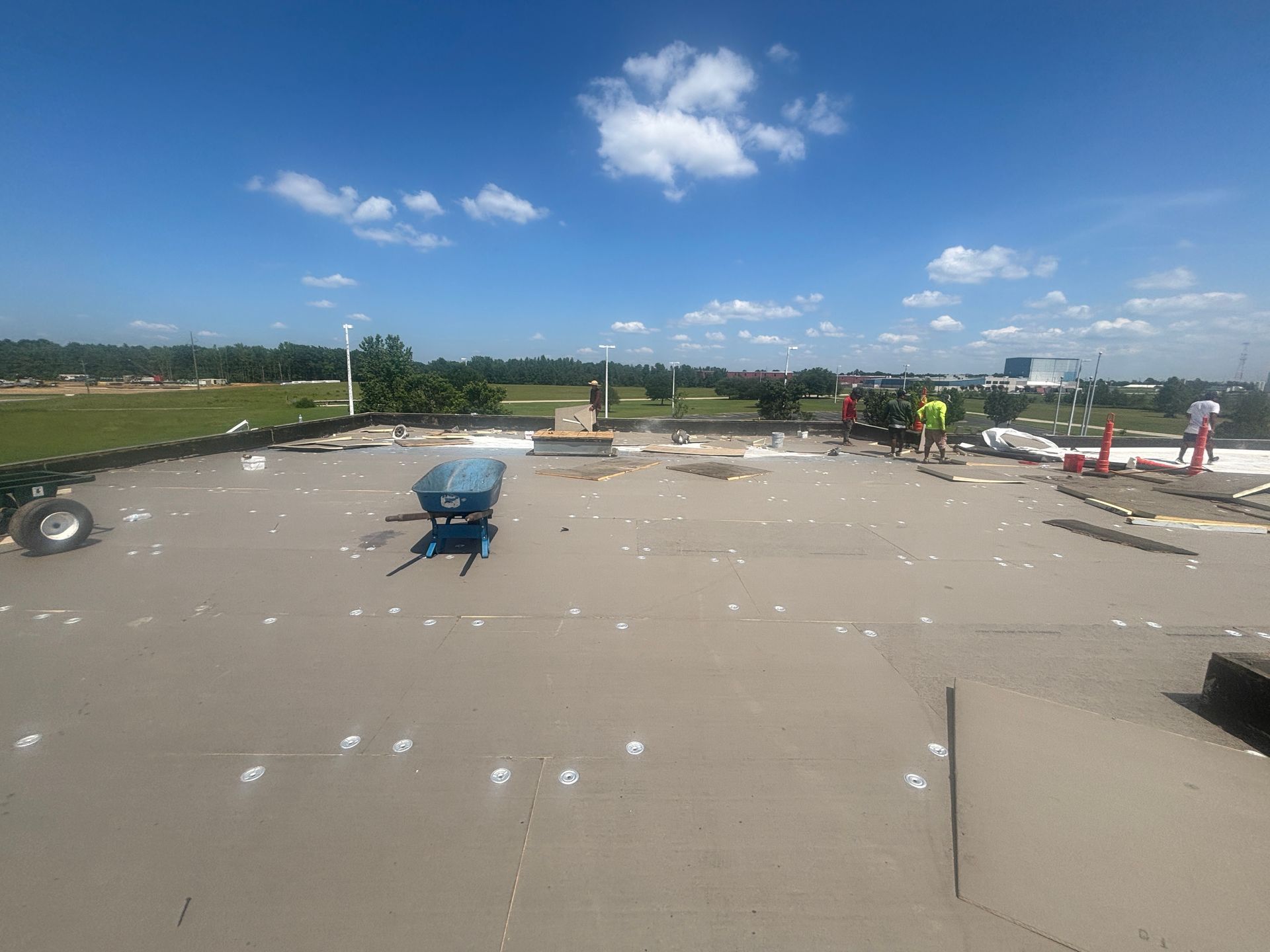 Workers on a flat roof under a blue sky, some near equipment.