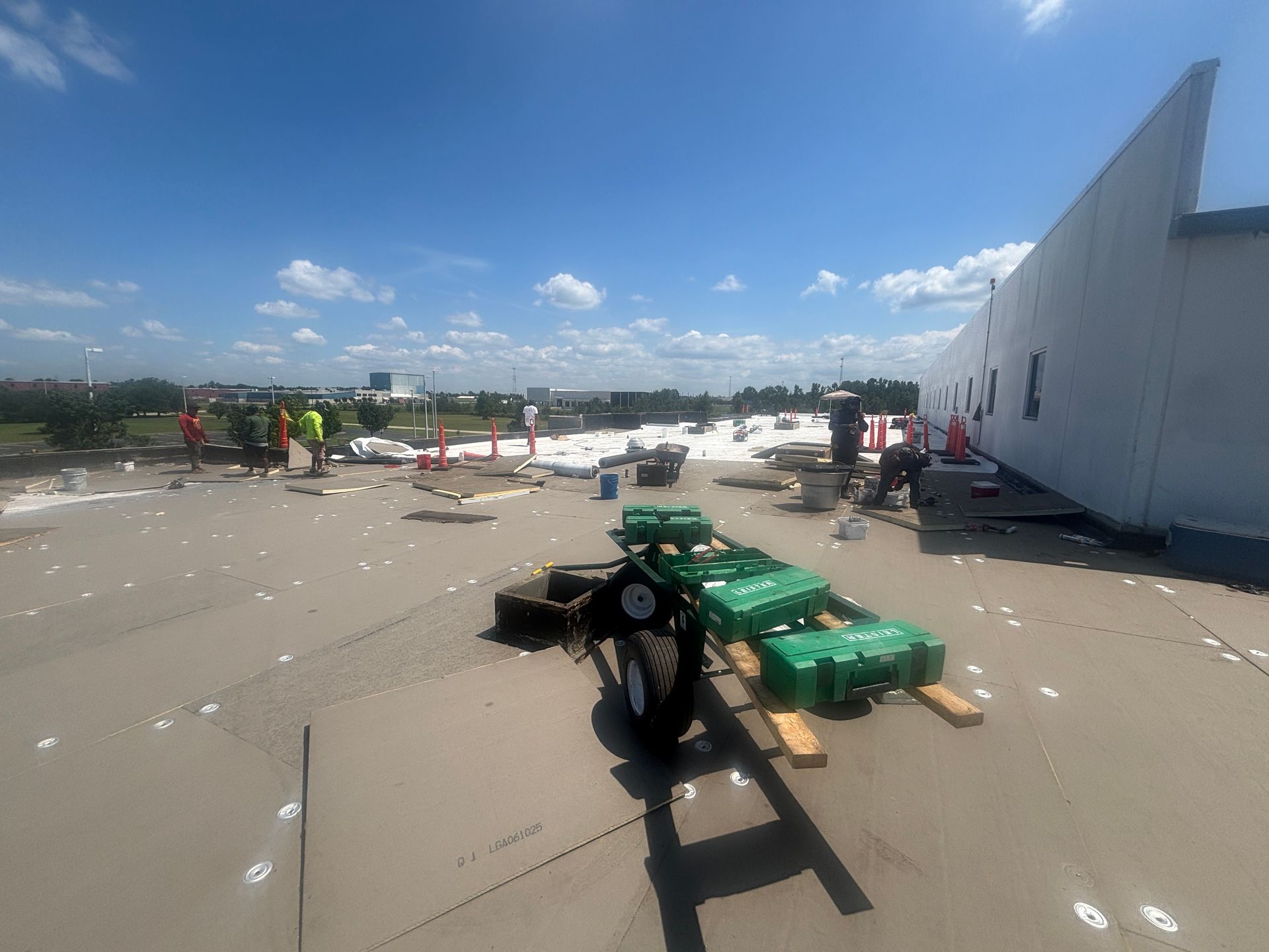 Construction workers on a flat roof under a blue sky, handling materials.