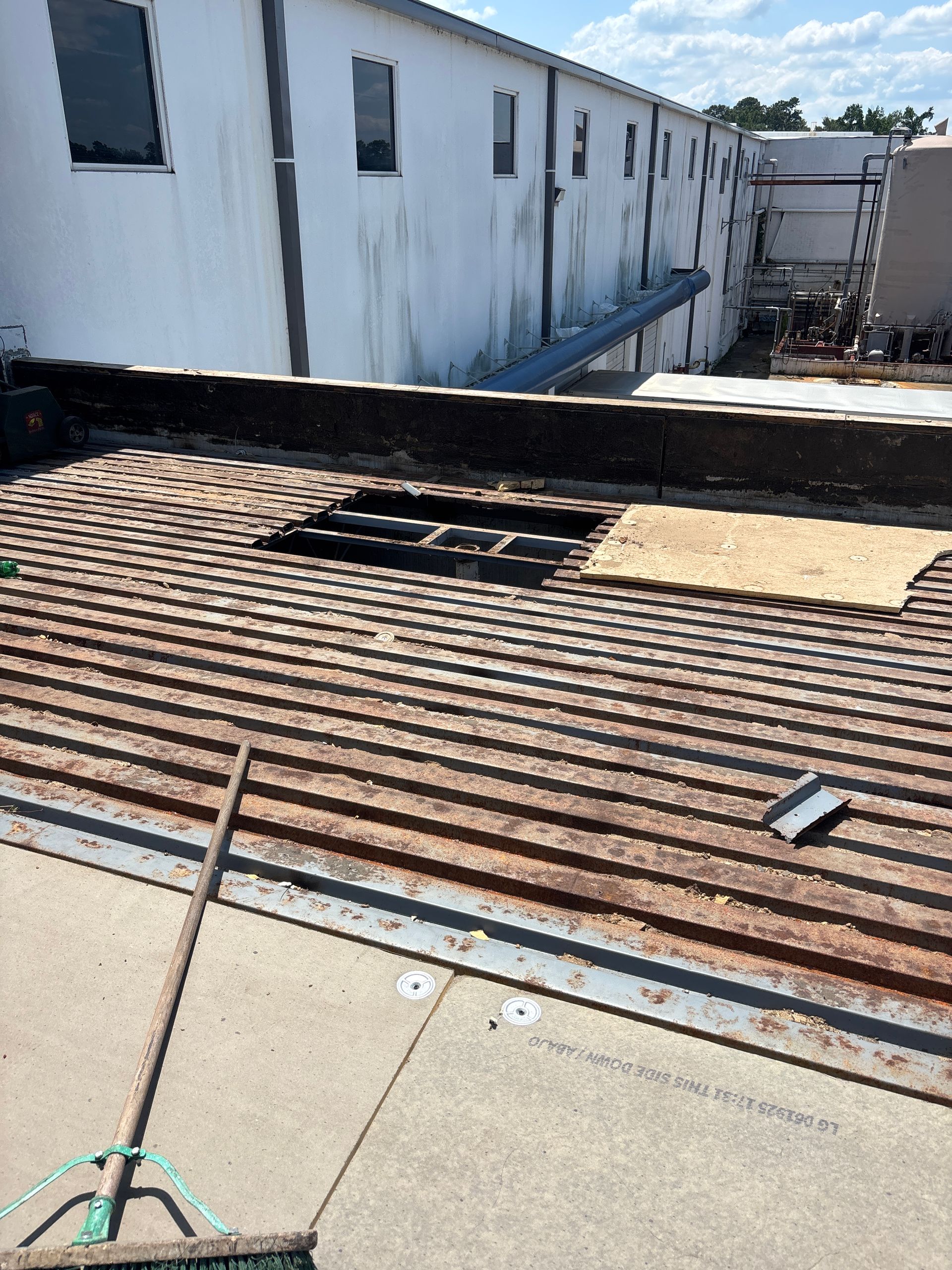 A rusted corrugated metal roof with a missing section, in front of a white building.