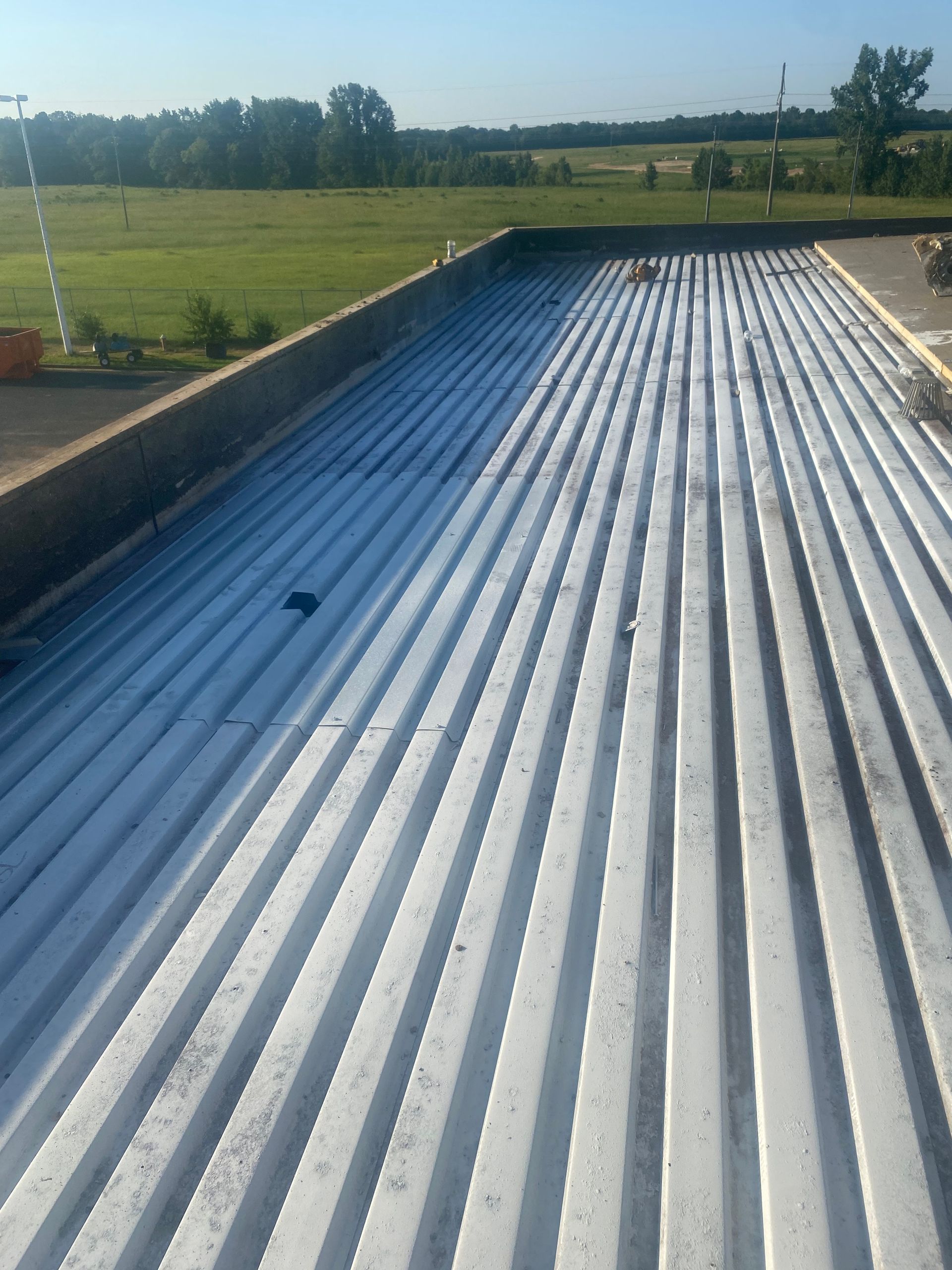 A corrugated metal roof, partially painted white, overlooks a grassy field under a blue sky.