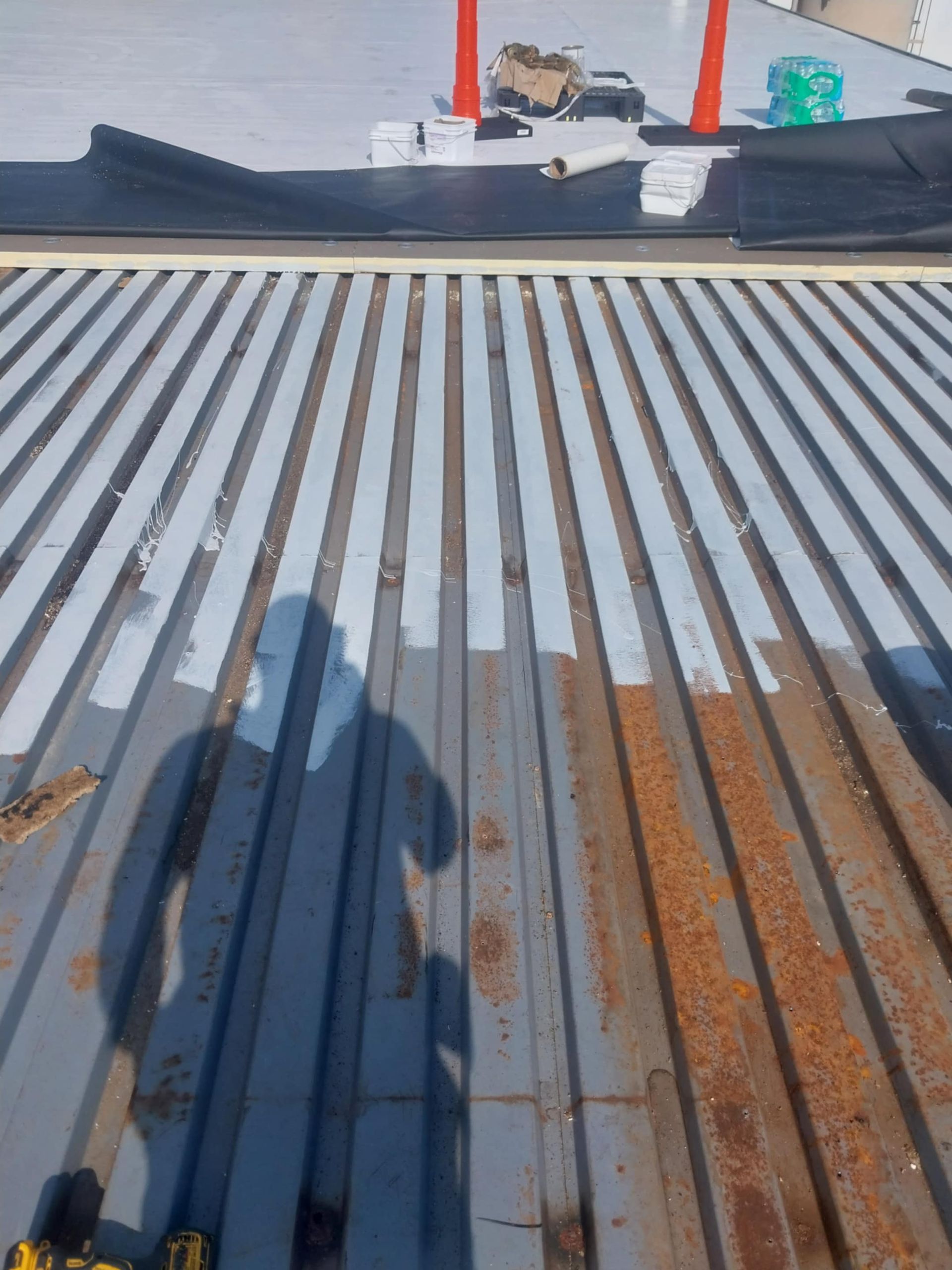 Metal roof with rust and fresh paint, person's shadow visible.