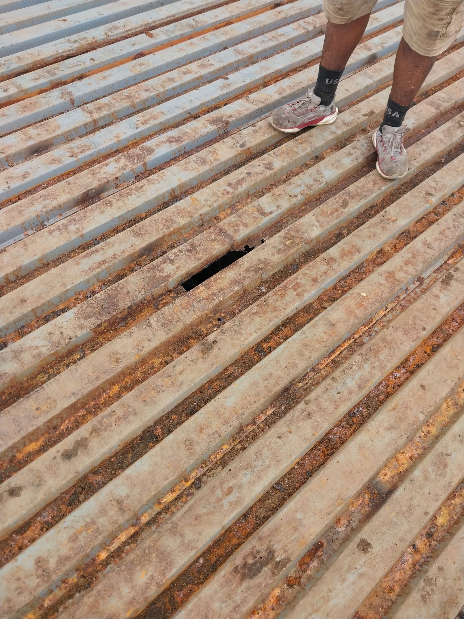 Person standing on a rusty metal surface with a hole.