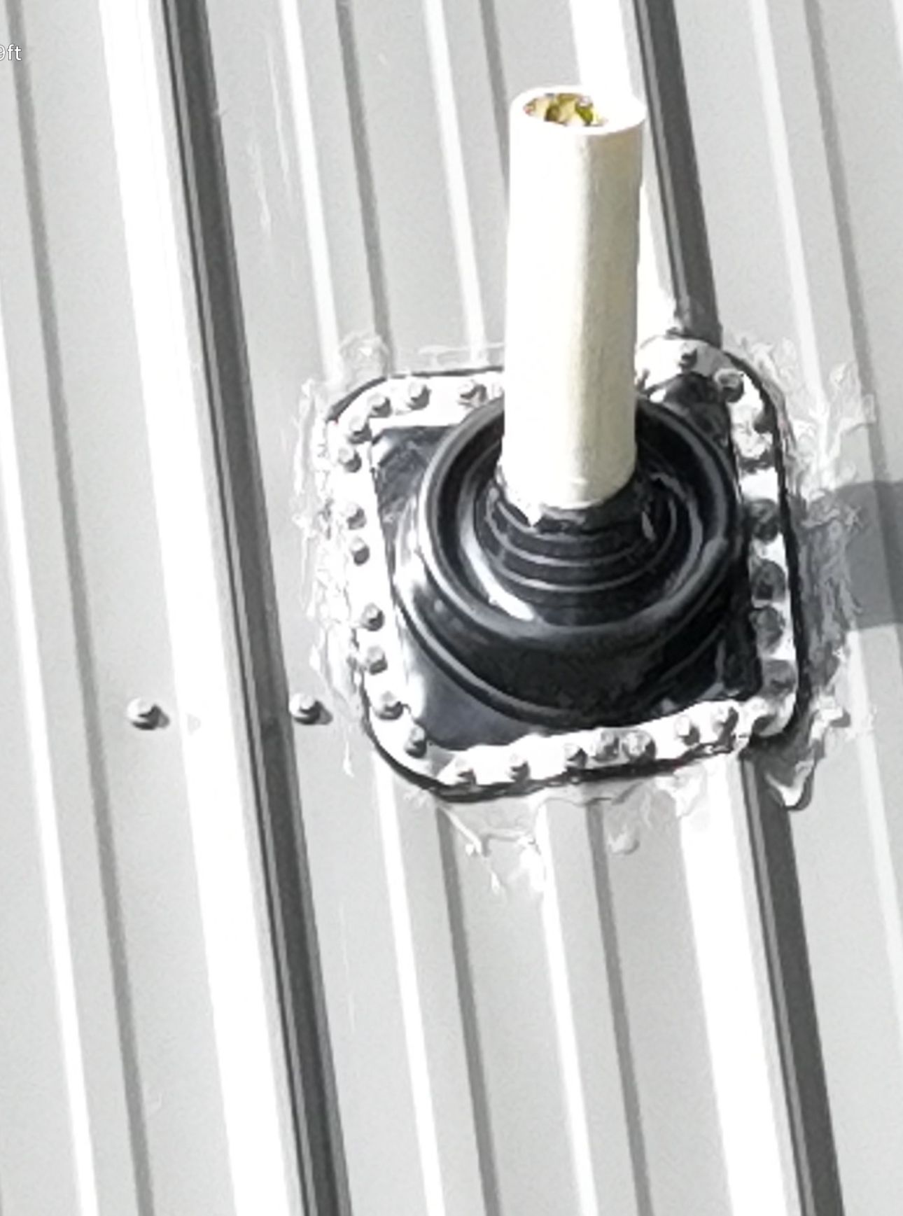 White pipe protruding from a metal roof flashing, secured with screws and sealant.