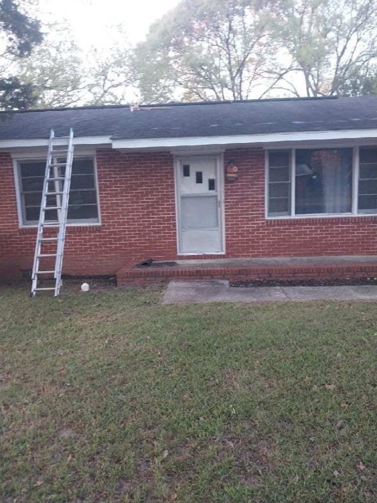 Brick house with a ladder leaning against the roof. A front door is in the center and windows on either side.
