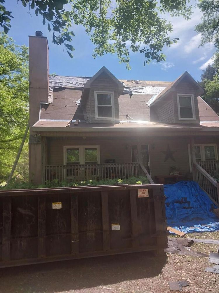 House with roof partially removed, dumpster in front, blue tarp on the ground.