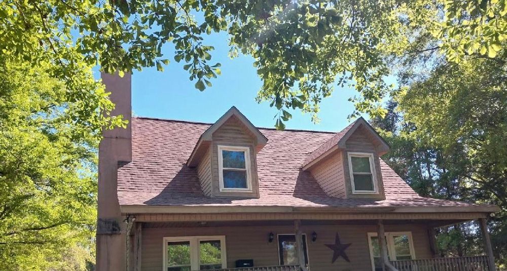 House with brown roof, two dormers, and a chimney; tree branches frame the blue sky.