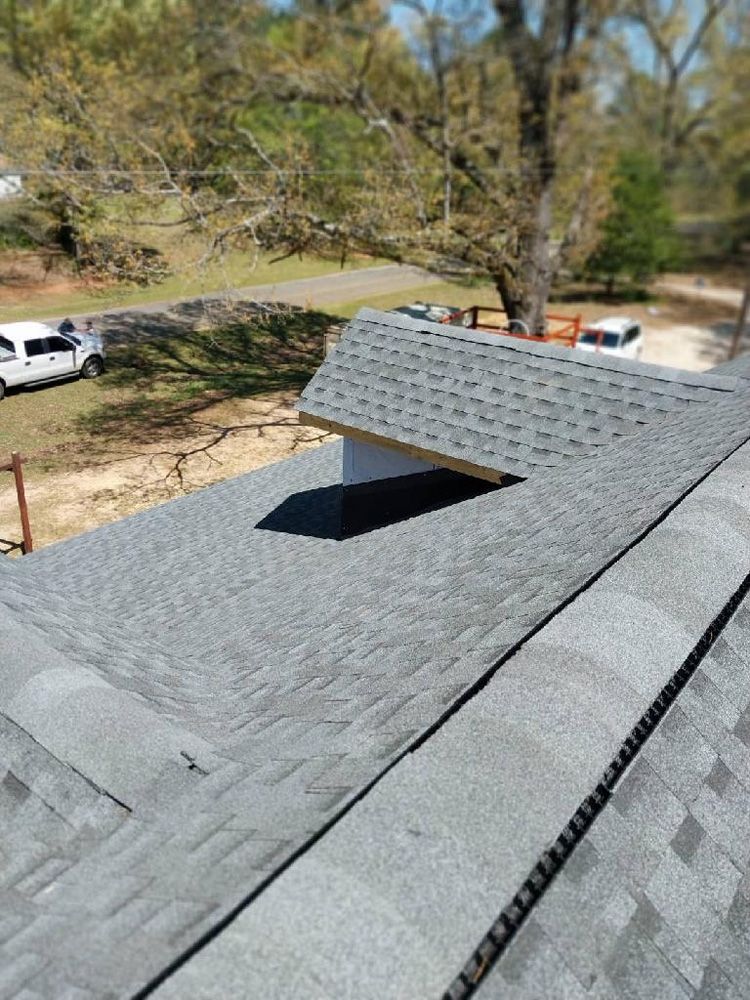 Gray shingle roof with an opening, viewed from above, with a background of trees and vehicles.