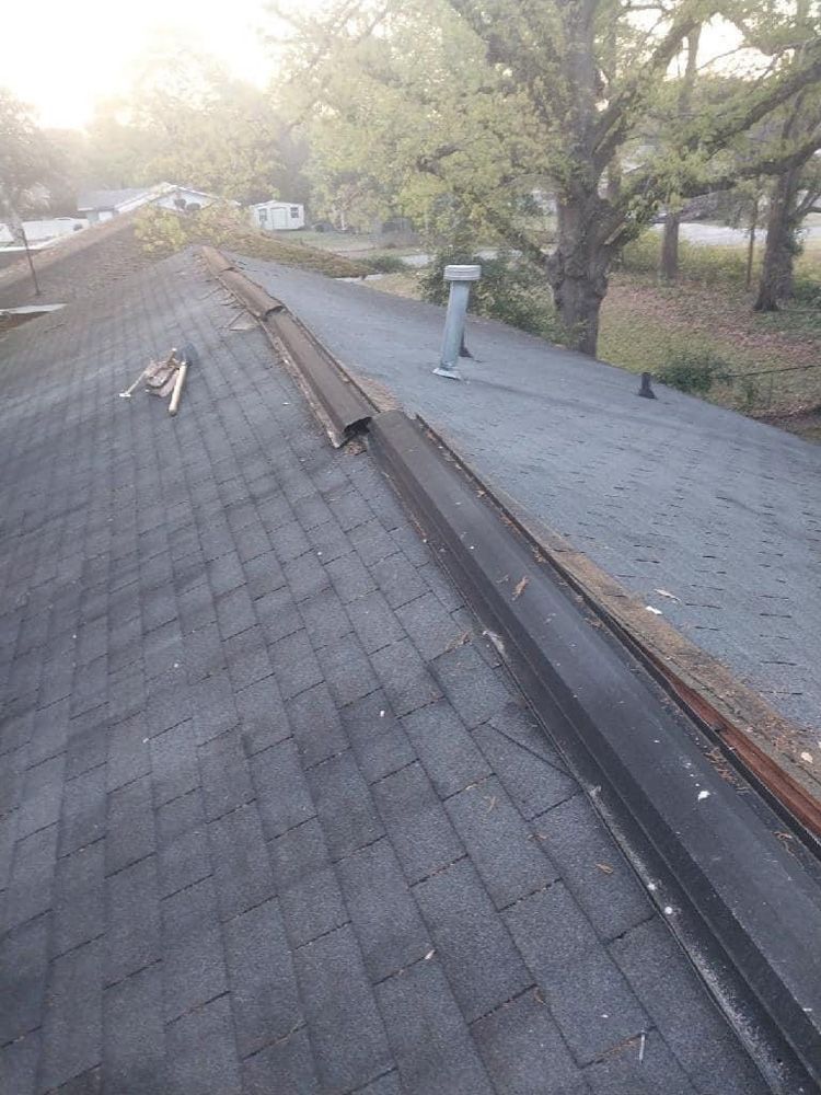 Overhead view of a dark shingle roof with a damaged metal flashing along the ridge.