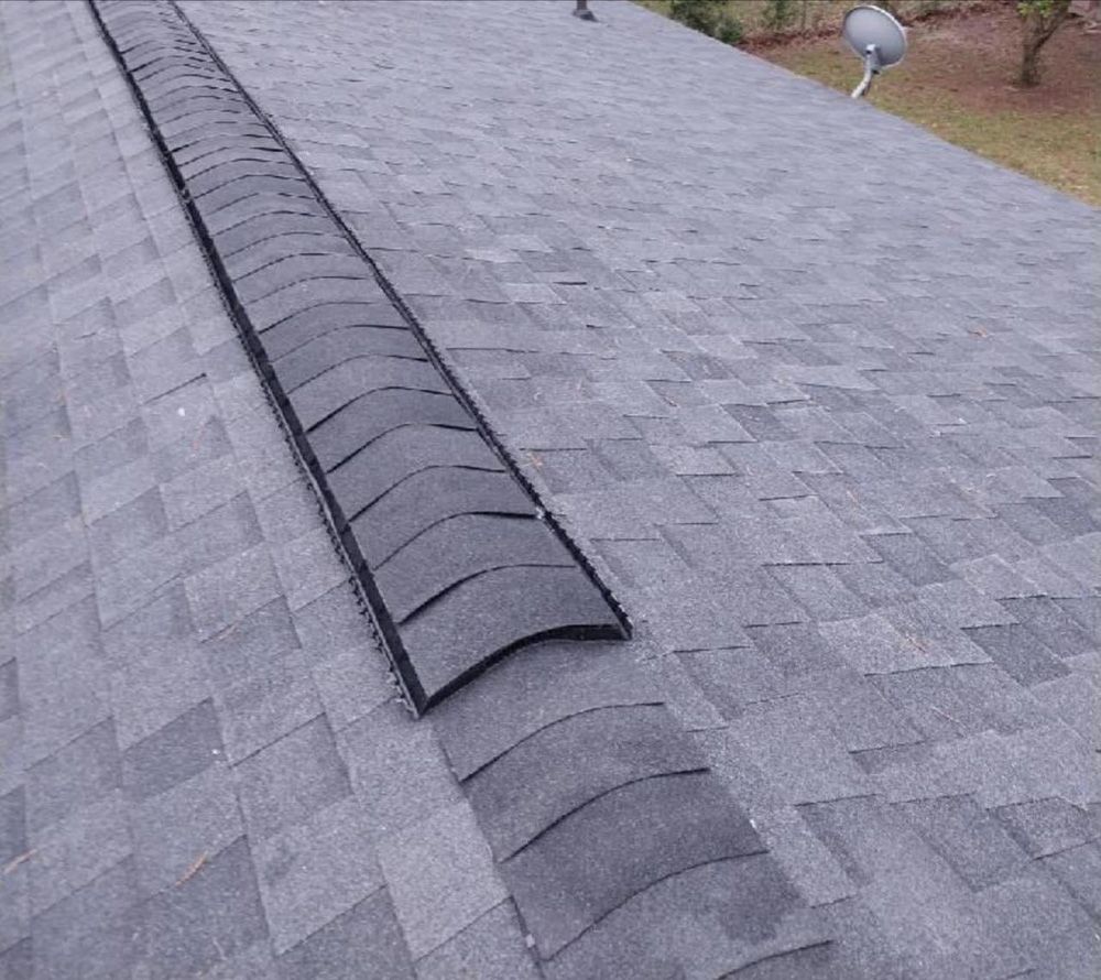Gray asphalt shingle roof with a dark ridge cap, outdoors.