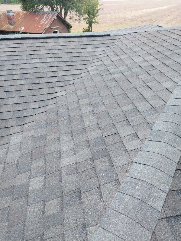 Gray shingled roof with a valley and other buildings in the background.