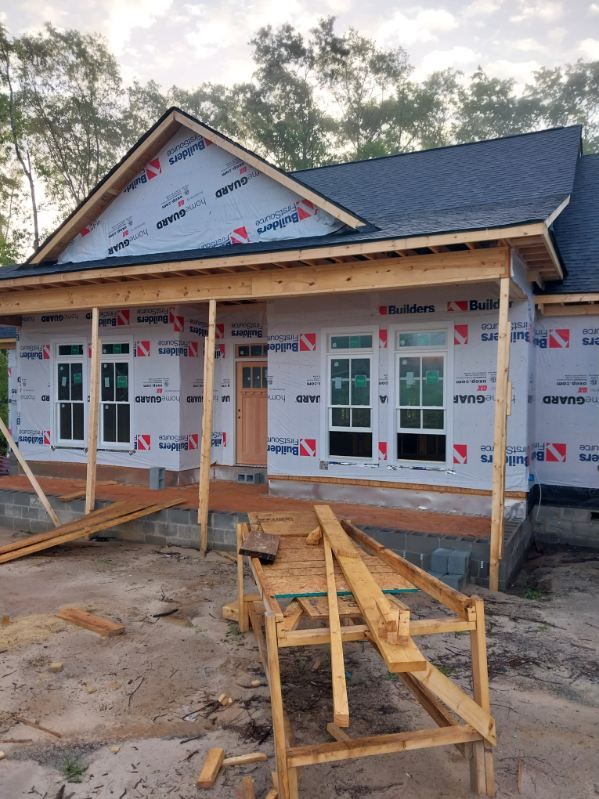 New house under construction with porch, blue roof, windows, and wood framing.