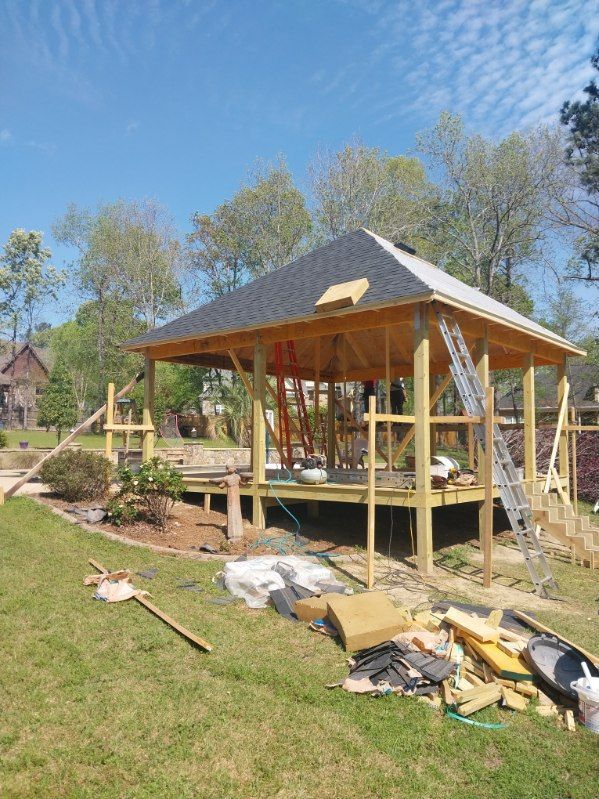 Wooden gazebo under construction with shingled roof, on a lawn, sunny day.
