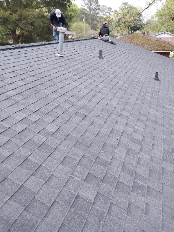 Two people working on a dark gray shingle roof outdoors.
