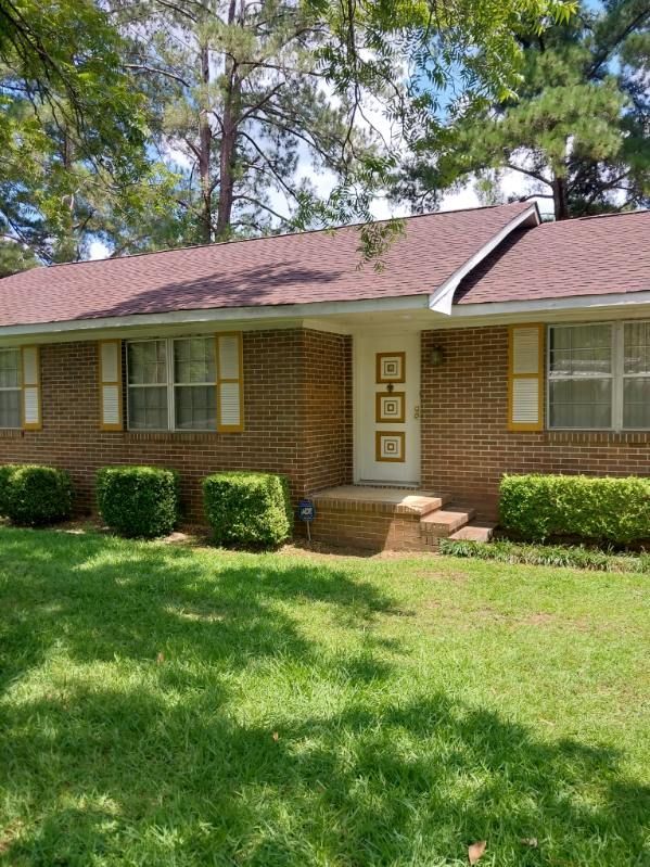 Brick ranch-style house with yellow shutters, a brown roof, and green lawn.