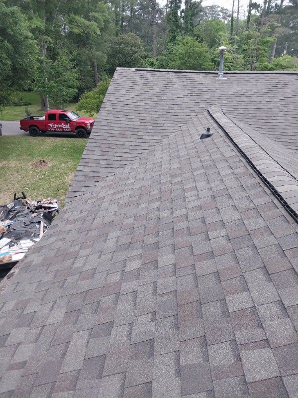 Roof with asphalt shingles, angled with a red truck on the side, trees in the background.