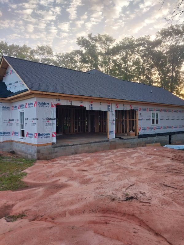 Garage under construction; exterior view with roof and frame visible. Wrapped in blue paper, on a dirt lot.