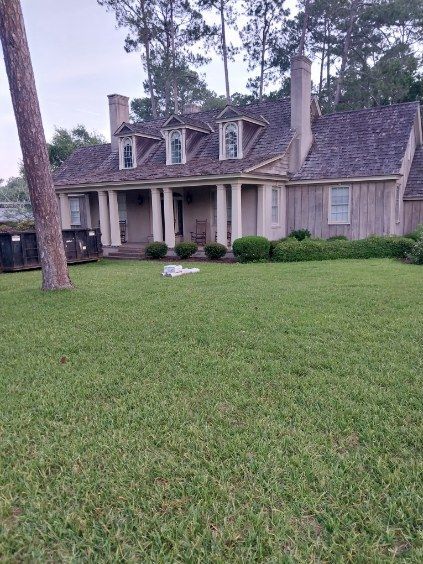 A light-colored house with a grassy front yard, trees, and a wooden shingle roof.
