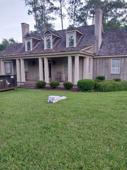 House with gray shingles, porch with white pillars, three dormers, and green lawn.