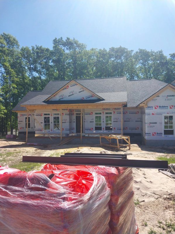 A partially constructed house with a dark roof and white siding is wrapped in protective material.