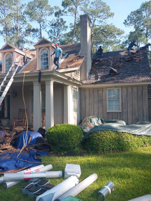 Roofers working on a house with a chimney; blue tarps and materials on the lawn.