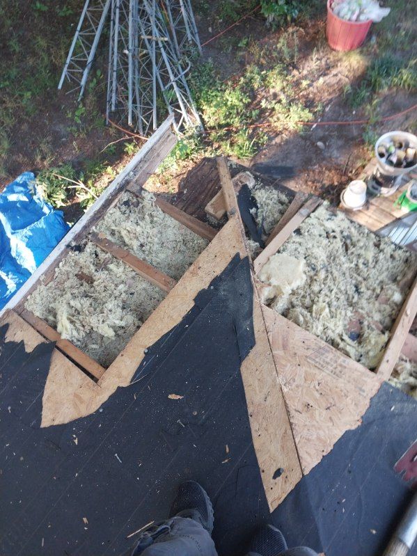 Rooftop with exposed insulation and damaged structure. Dark roofing material and debris present.