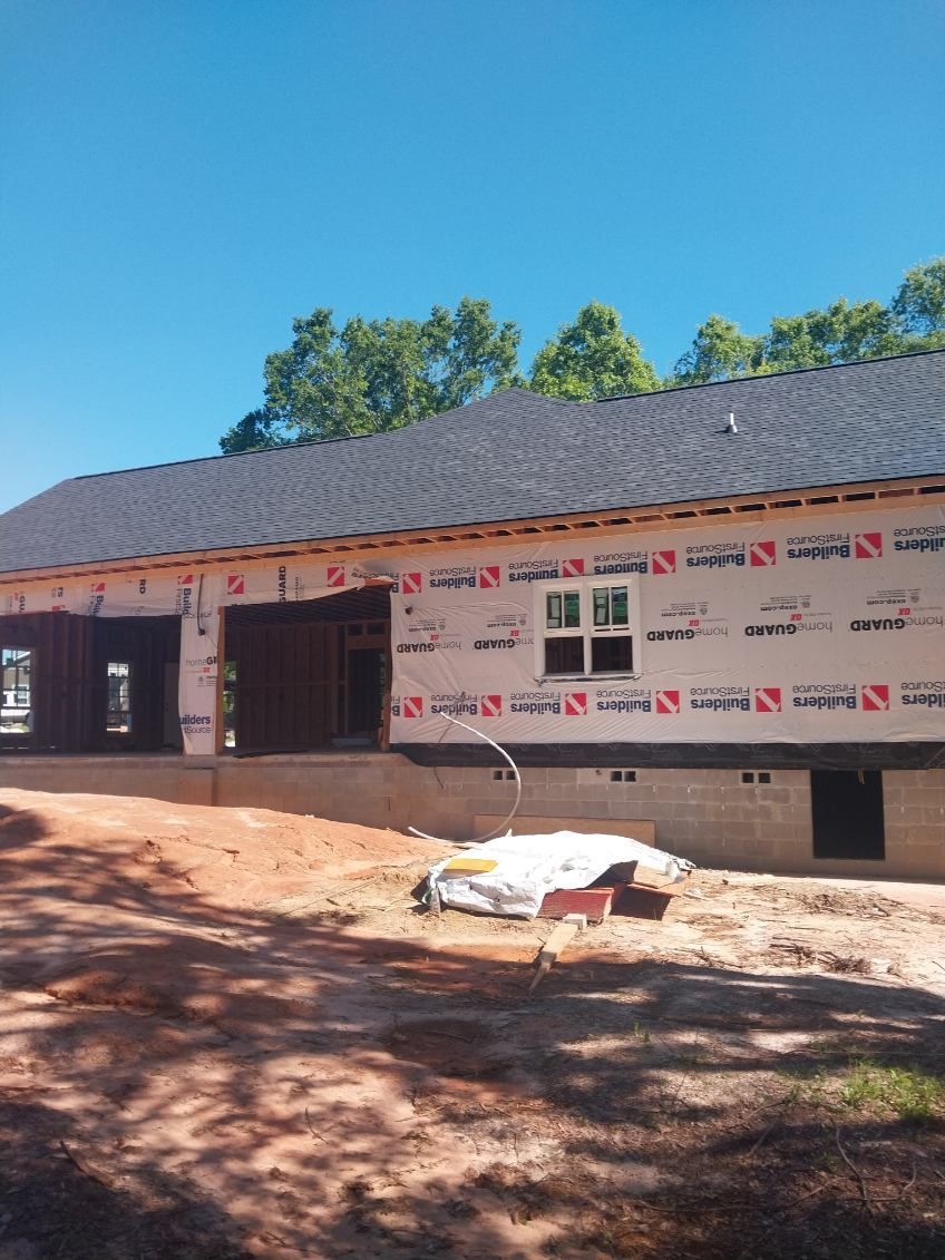 New house under construction with roof and wrap installed, sunny day.