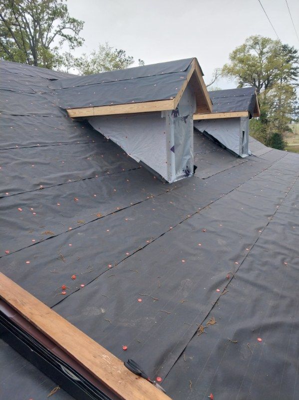 Rooftop with black underlayment and two unfinished dormers with exposed wood frames.