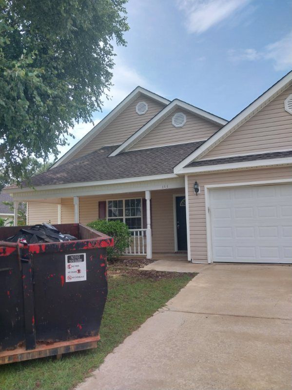 Tan house with dark roof and white garage door; a dumpster sits in the yard.