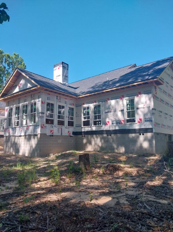 House under construction with windows, roof, and chimney against a blue sky.