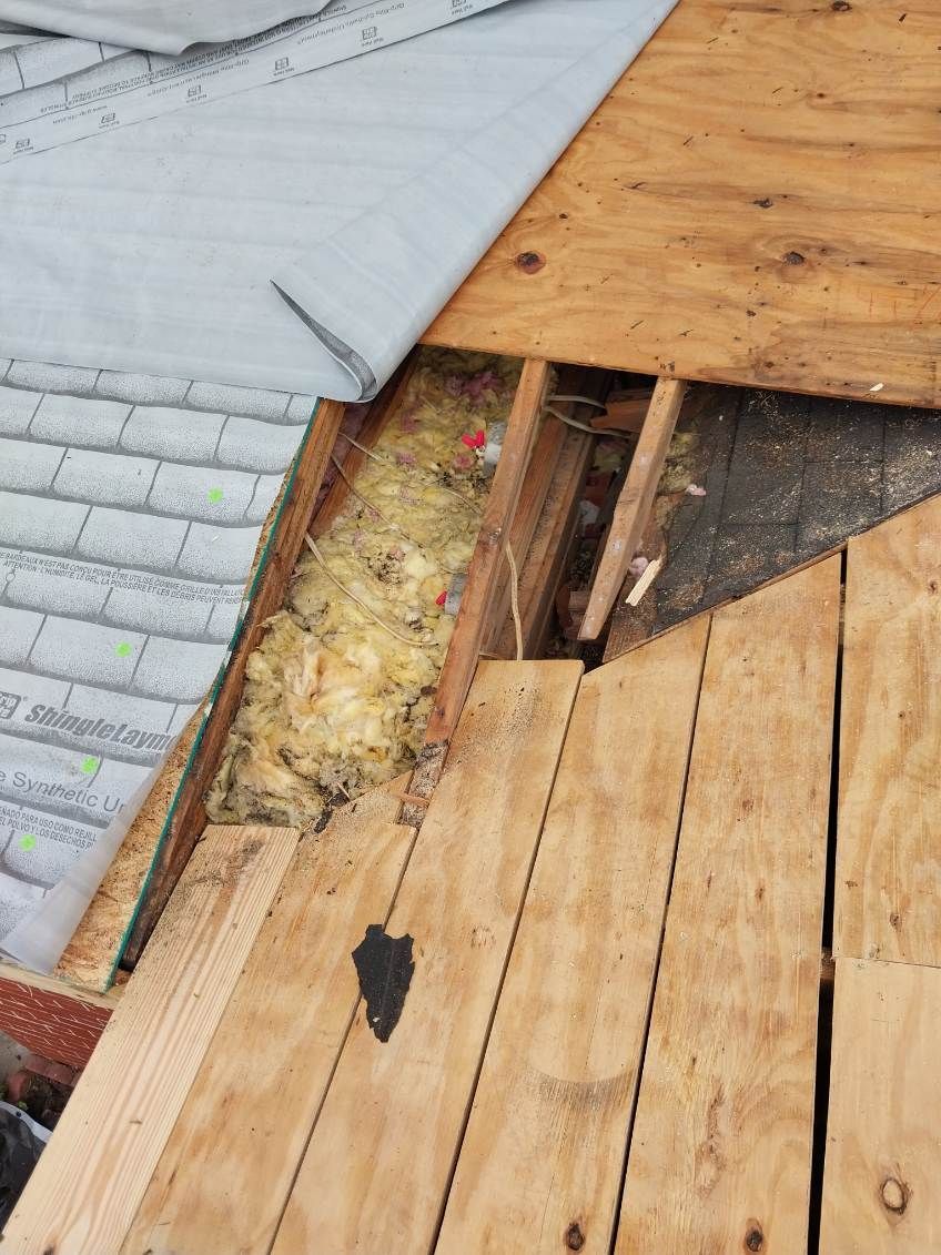 Damaged roof showing missing shingles, exposed plywood, insulation, and underlayment.