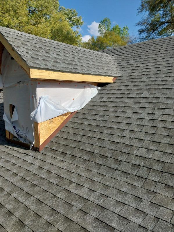 Newly constructed dormer on a shingled roof, wrapped in white material.