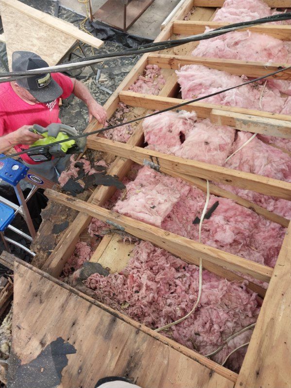 Person using a power saw to cut into a partially constructed roof with pink insulation visible.