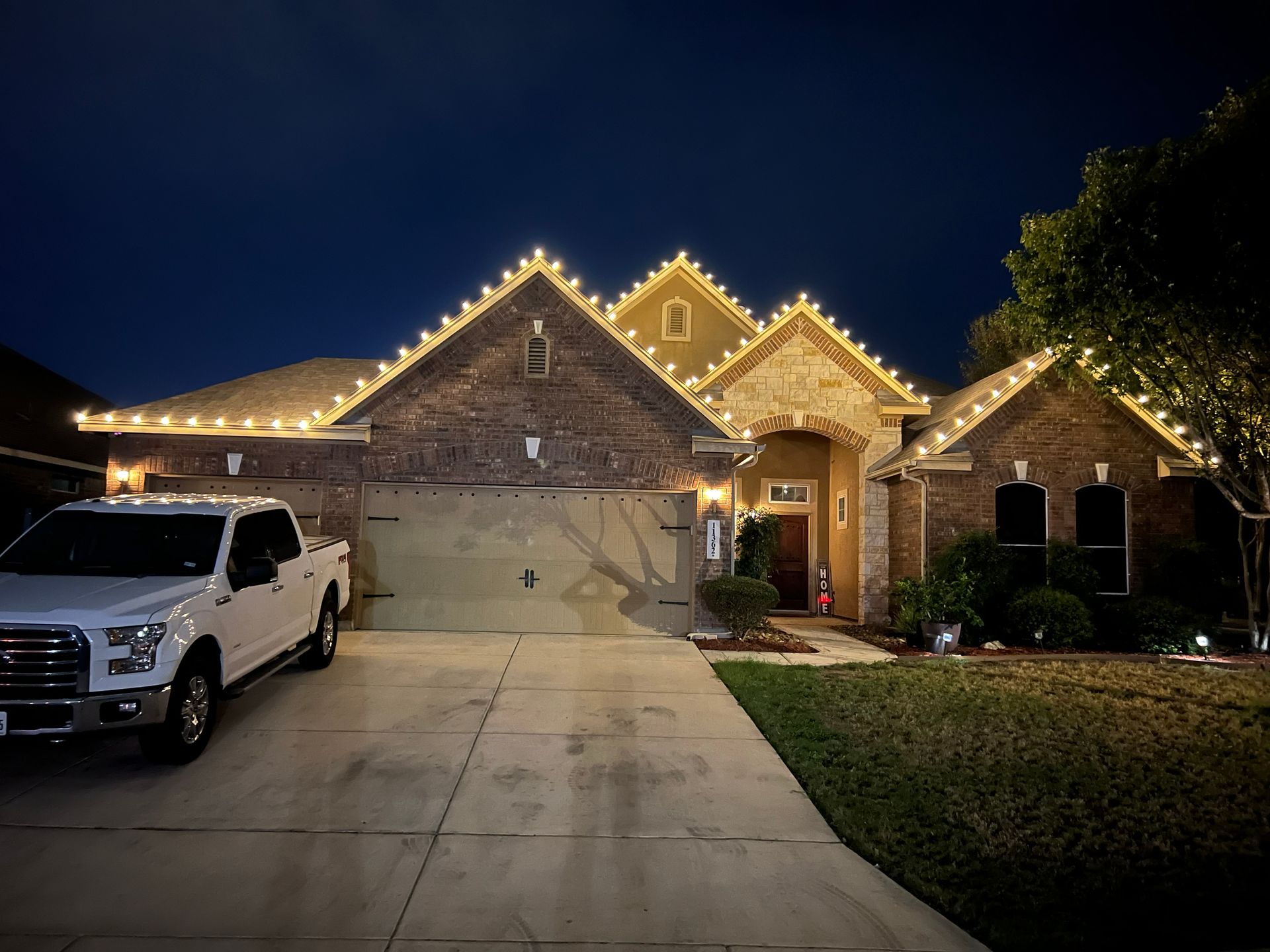 House with Christmas lights outlining the roof, a white truck parked in the driveway at night.
