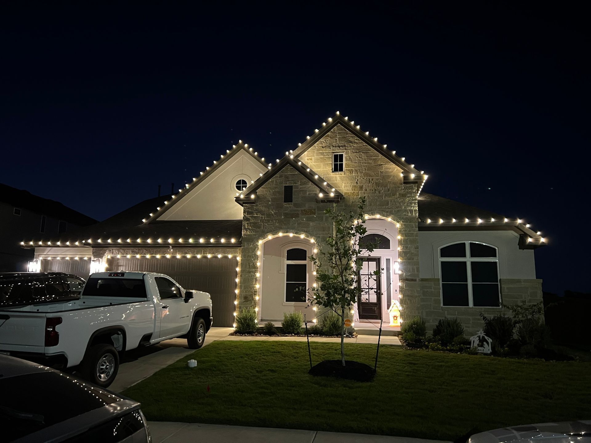 House decorated with white Christmas lights at night, white truck parked in front.