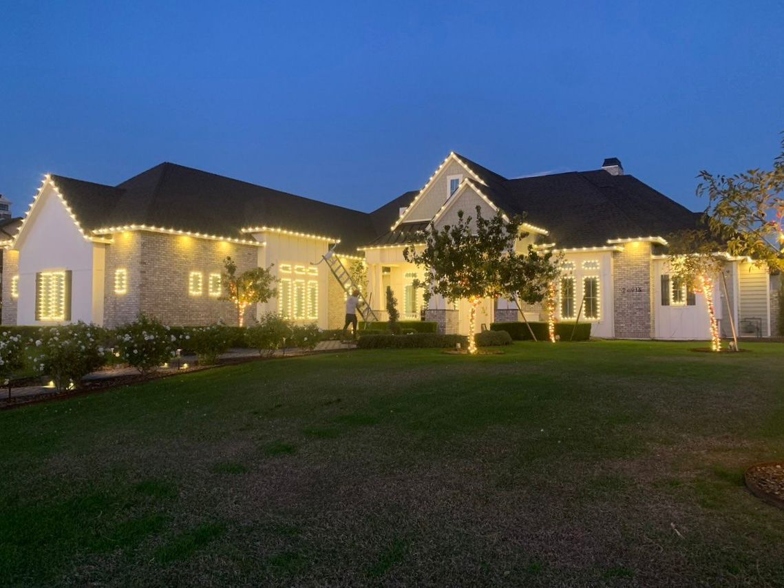Large house illuminated with white lights against a dusky blue sky; lawn in foreground.