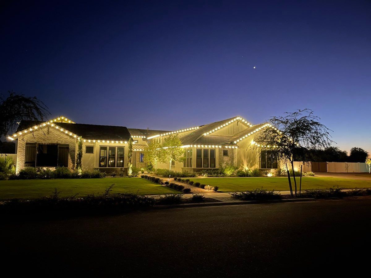 House at night with warm white lights along the roof and windows, and on a tree.