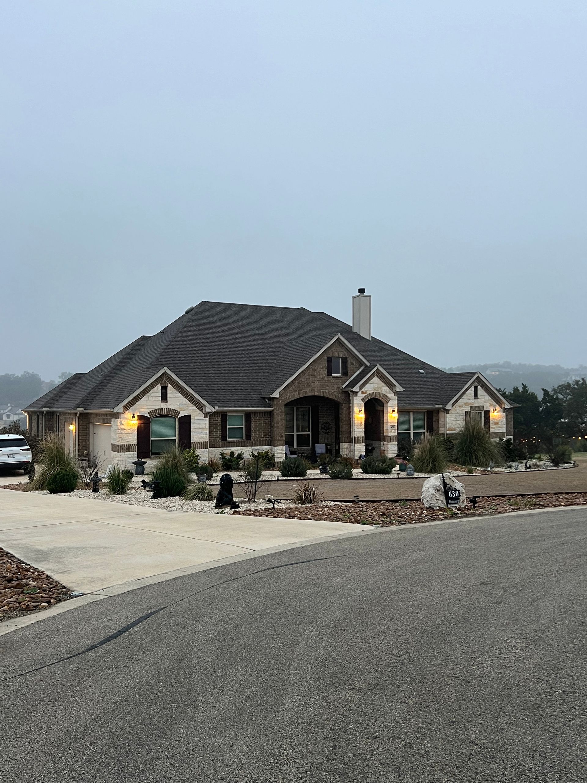 Single-story brick home with dark roof, light-colored stone accents, and a gravel driveway on a cloudy day.
