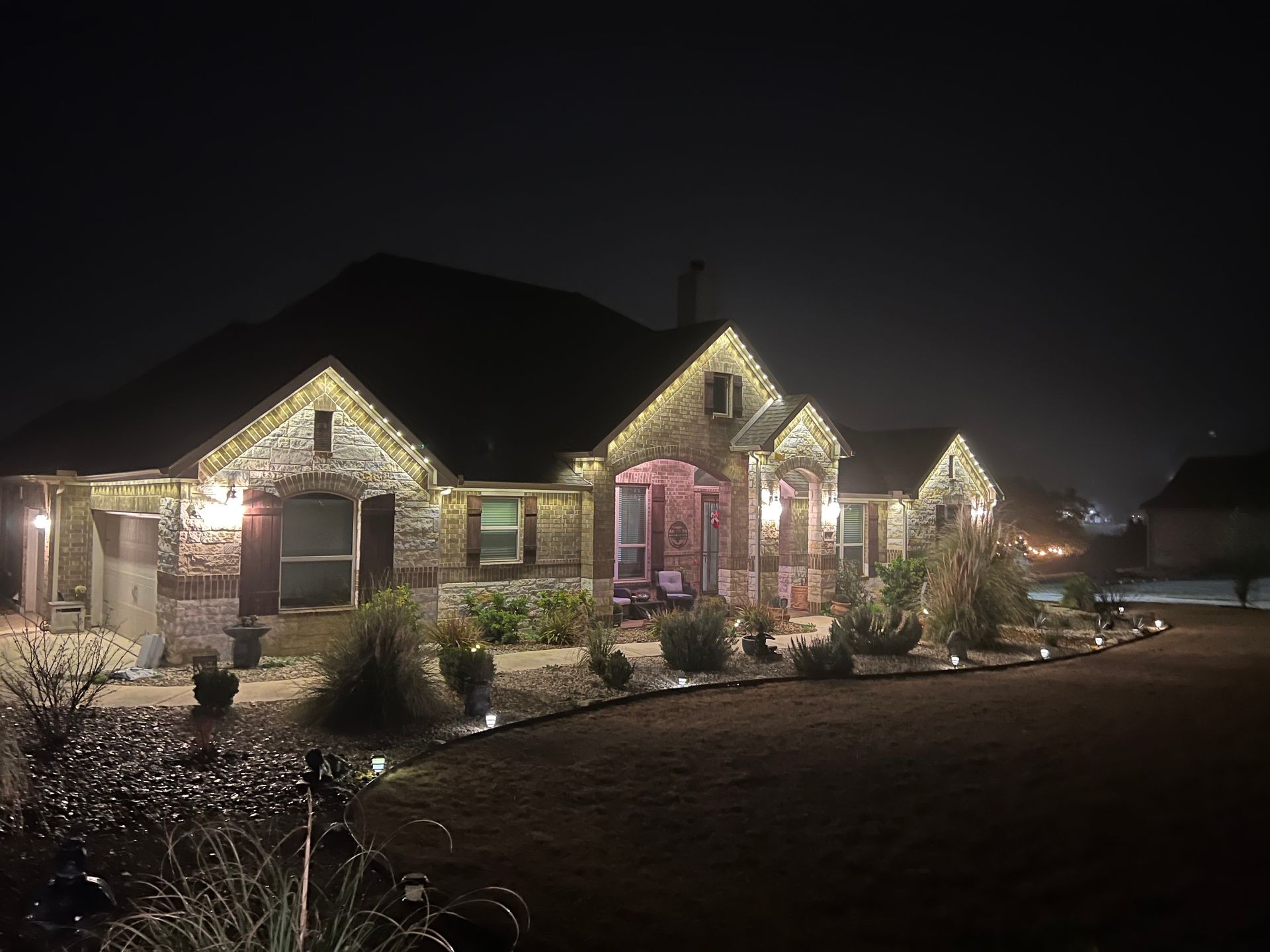 House at night, decorated with lights, illuminated lawn and bushes.