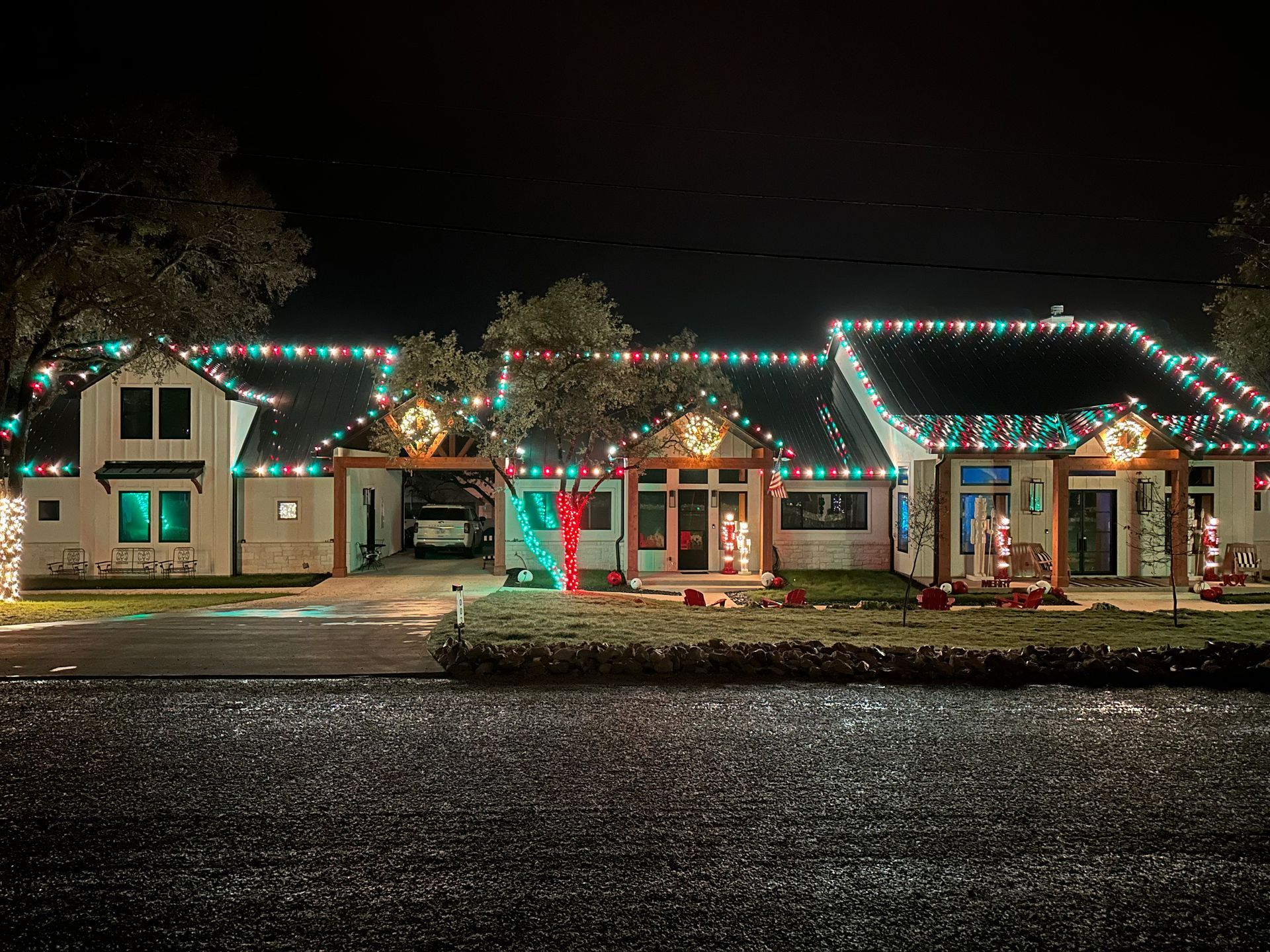 House decorated with Christmas lights at night. Green, red, and white lights, wreaths, and lawn ornaments.