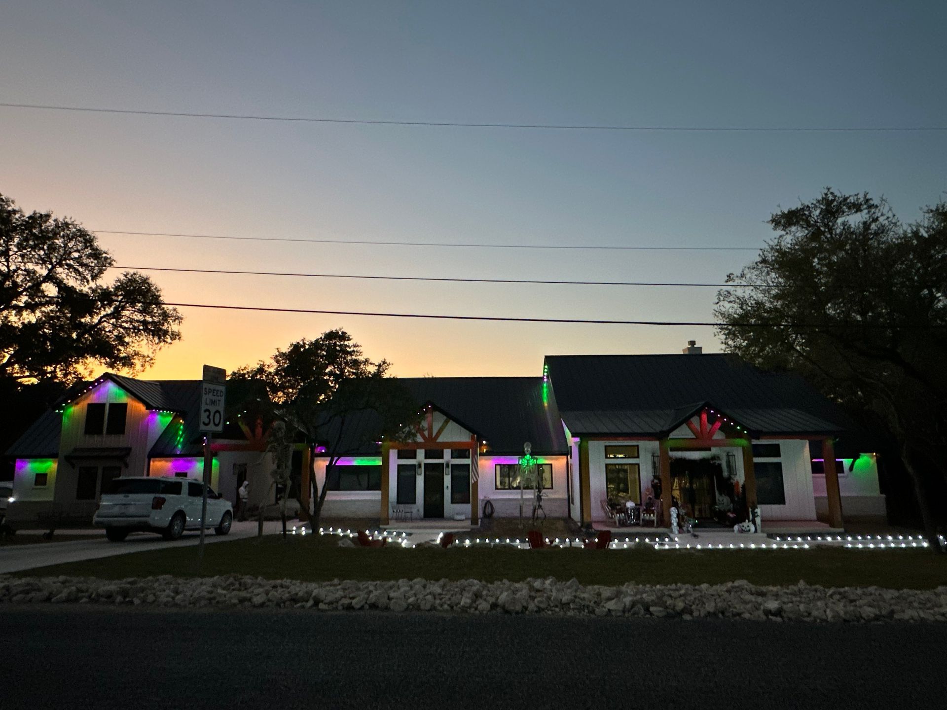 Houses with Christmas lights at dusk; green, purple, and white lights illuminate the buildings.