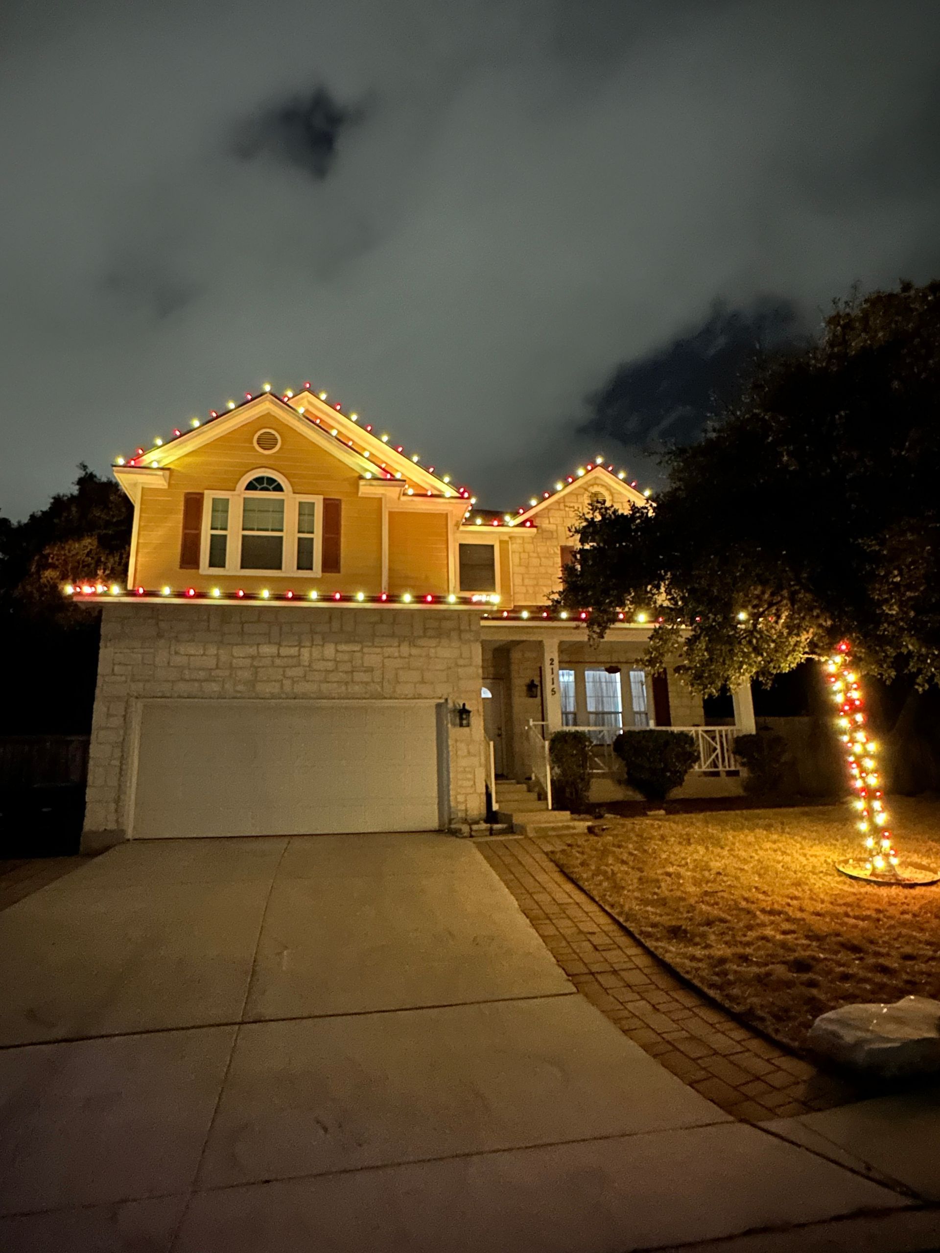 House decorated with Christmas lights at night. The roof and tree trunk are wrapped in warm-colored lights.