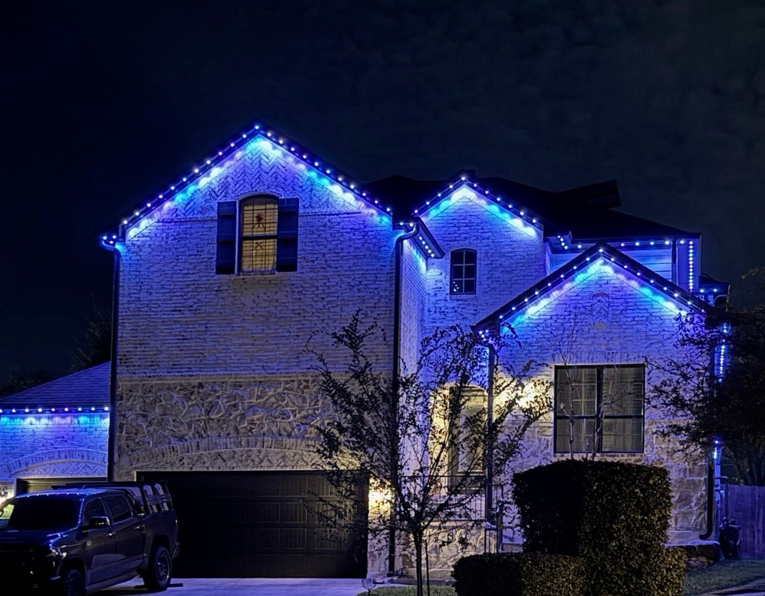 House with blue Christmas lights on the roof at night; gray car in the driveway.