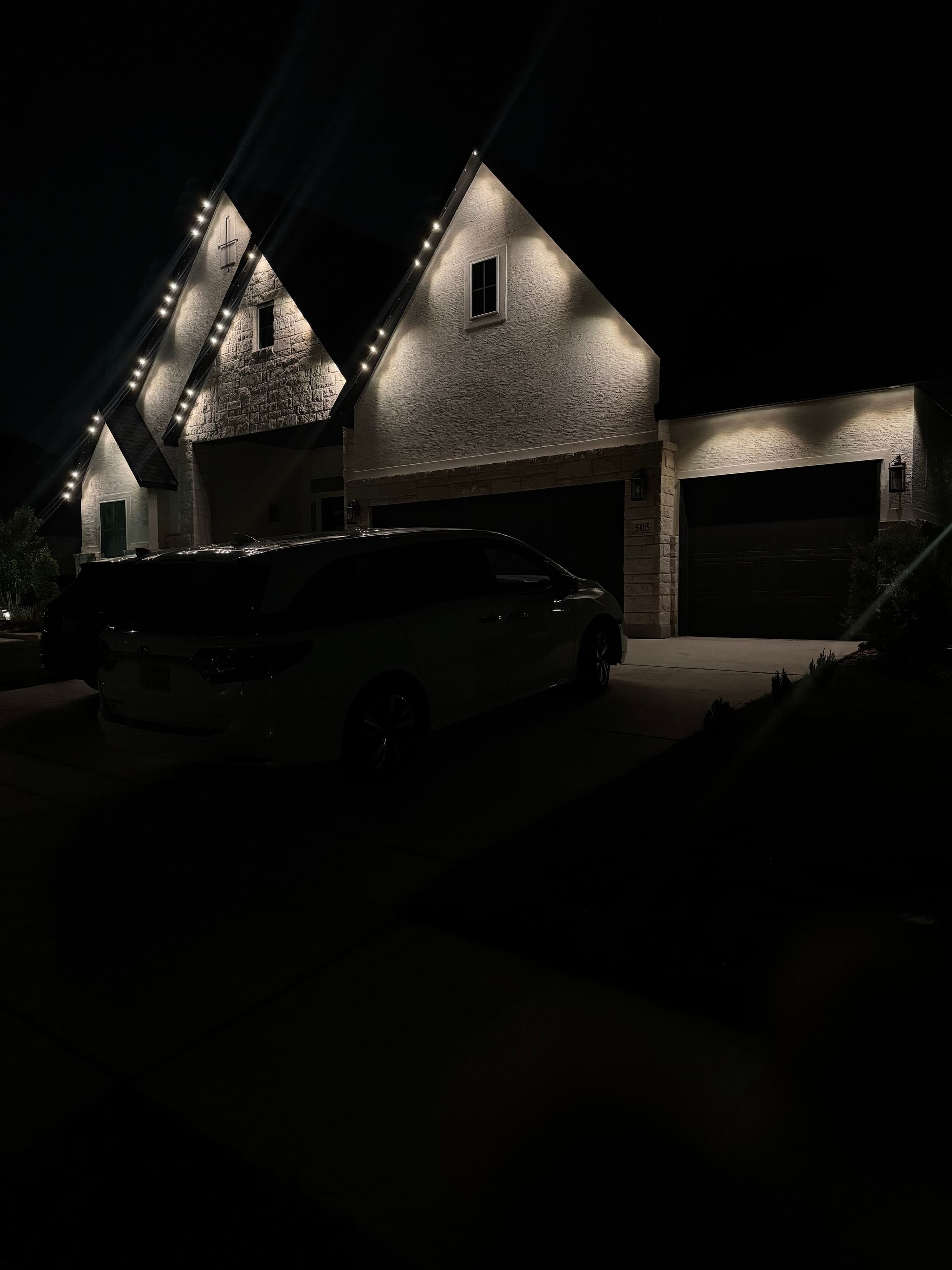 Night view of a stone house illuminated by lights, with a vehicle parked in front of the garage.
