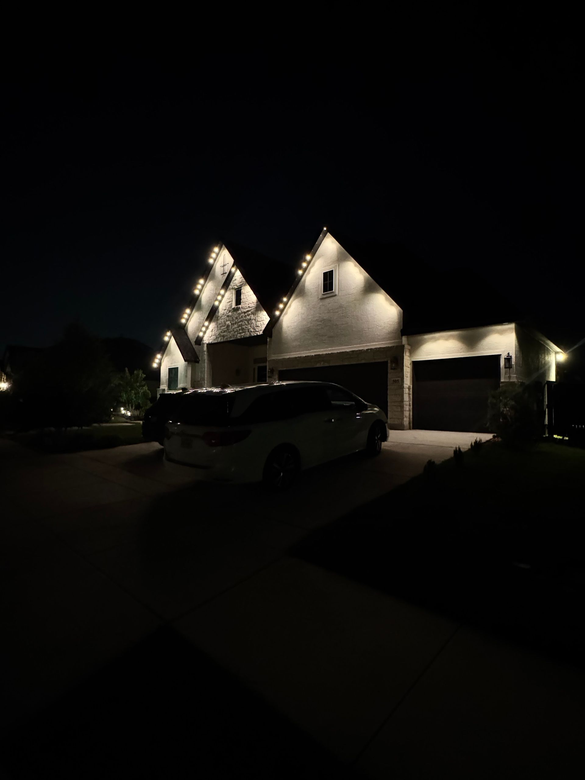 House at night with Christmas lights and a car in the driveway.